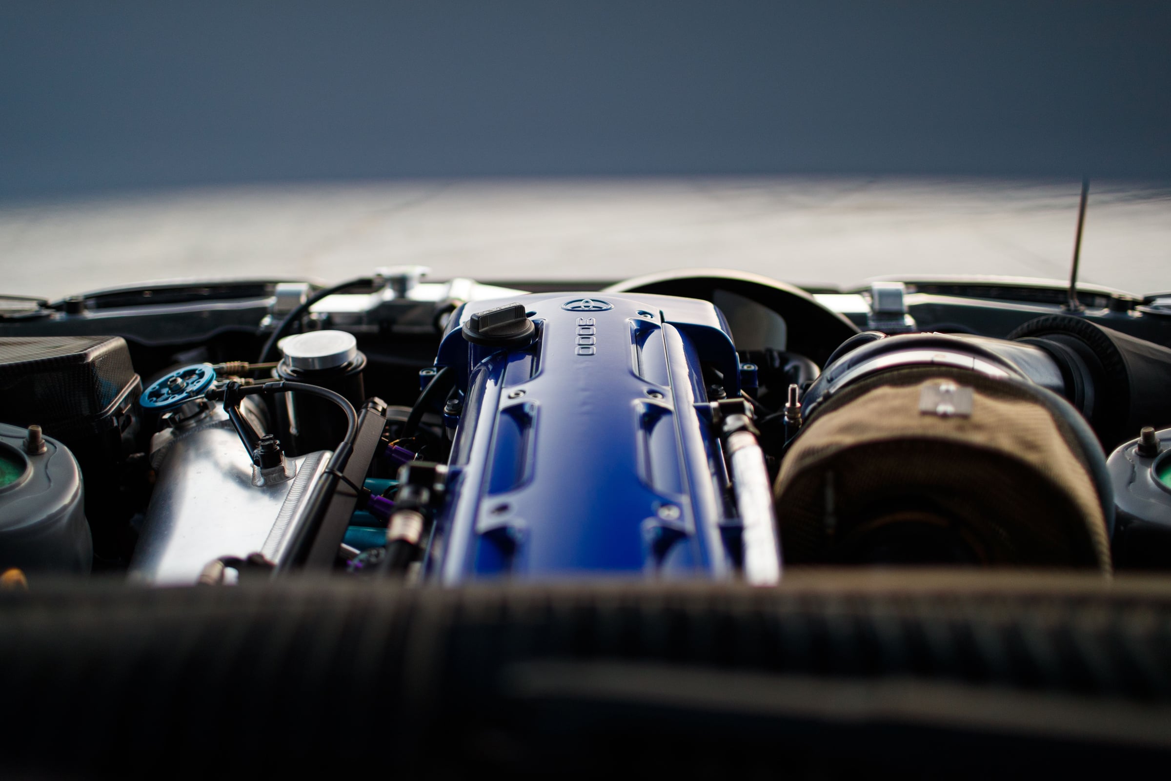 Gros plan sur la baie moteur d'un six-cylindres Toyota 2JZ : cache-culbuteurs bleu marqué « 3000 », gros turbo sous protection thermique à droite.